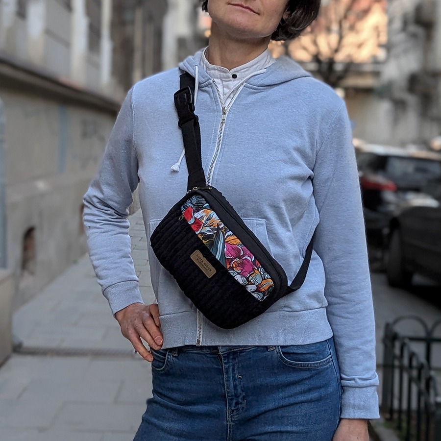 Ręcznie szyta szaro-czarna saszetka z pionowym wzorem i florystyczną wstawką, na tle miejskiego muru