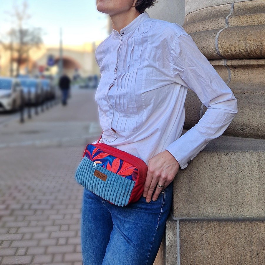 Ręcznie szyta nerka damska z czerwonym paskiem, wykonana z niebieskiego sztruksu tapicerskiego i materiału z czerwono-granatowym motywem liści noszona na biodrach